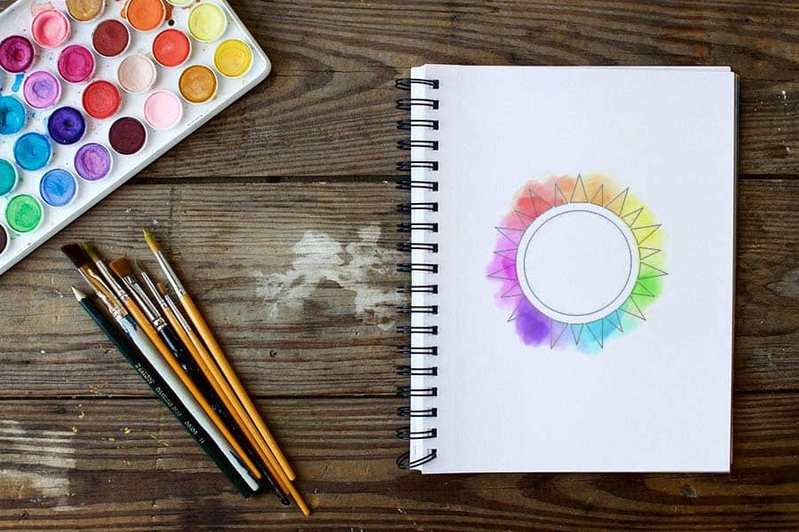 A drawing of a color wheel with various paints on a notebook.