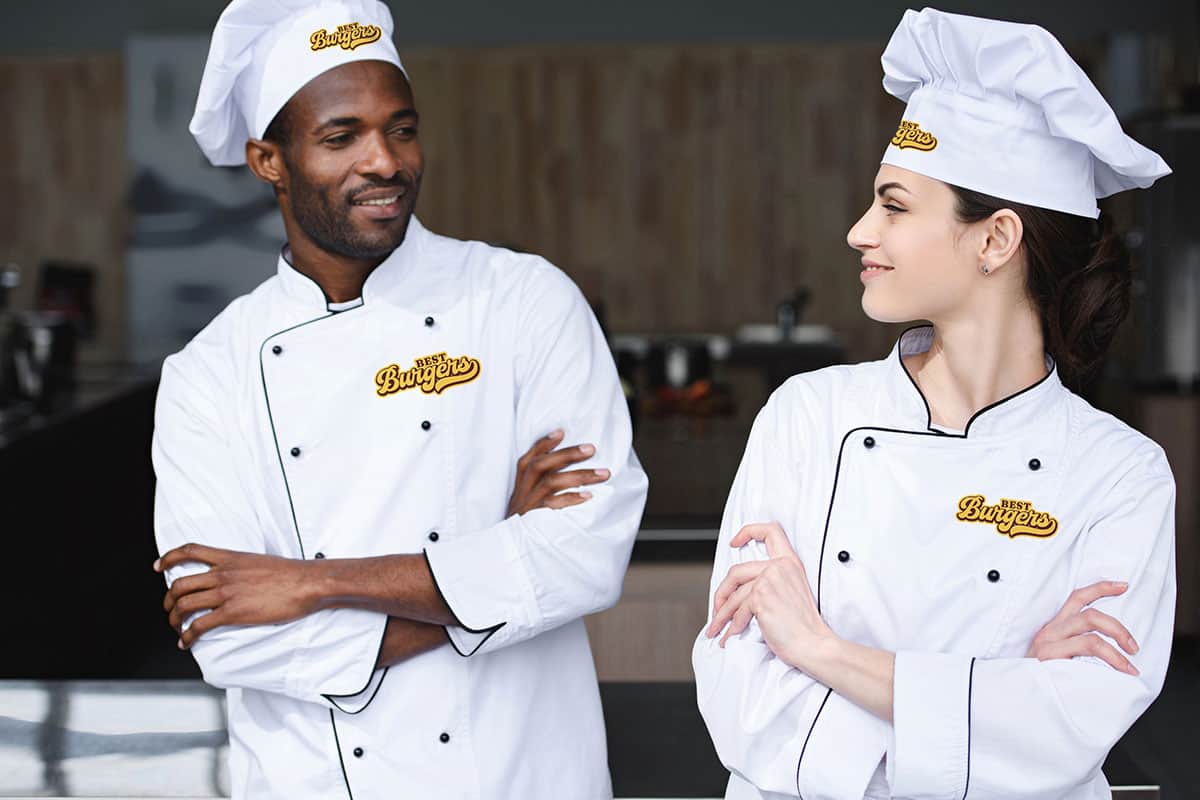Branded Chef Uniforms Chefs in San Antonio custom apparel smiling in a modern kitchen.
